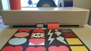 Plotter de découpe sur un établi, une planche de stickers aux formes colorées fraîchement découpées au premier plan