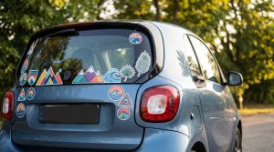 Hayon arrière d'une petite voiture décoré de stickers vinyle colorés, motifs montagnes, vagues et feuillages